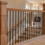 A carpenter secures a wood banister post and metal balusters at a stair landing while an inspector checks rail continuity.