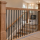A carpenter secures a wood banister post and metal balusters at a stair landing while an inspector checks rail continuity.