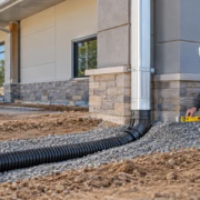 A site supervisor checks a commercial roof downspout connected to an underground storm drain graded away from the foundation.