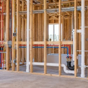 An inspector reviews plumbing, electrical, and HVAC rough-in systems exposed in open wall framing.