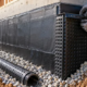 A worker installs dimpled drain board over waterproofing on a basement foundation wall above gravel and a footing drain.