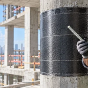 Engineer examines a fiber-reinforced polymer bar beside a concrete column strengthened with a carbon-fiber wrap.