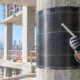 Engineer examines a fiber-reinforced polymer bar beside a concrete column strengthened with a carbon-fiber wrap.