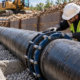 A construction crew inspects a ductile iron water main pipe joint in a protected utility trench.
