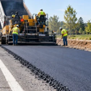 Road crew adds a new asphalt lane beside an existing road while an engineer checks the widened edge.