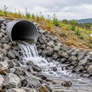 A drainage pipe daylight outlet releases water onto a rock-lined apron at a graded site.