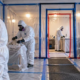 Remediation workers in protective suits remove material inside sealed plastic containment with HEPA negative-air equipment.