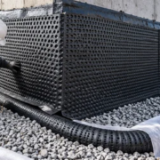 A site inspector checks dimpled drainage board meeting a gravel-wrapped foundation drain before backfill.