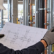 Plumbing technician reviewing a branch connection drawing beside installed water-service pipework.