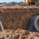 Surveyors checking the invert elevation of a stormwater pipe with a laser level and leveling rod in an excavation.