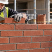 A mason and supervisor inspect a brick running bond wall with each course offset by one third of a brick length.