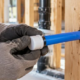 Plumber fitting an end cap onto a blue PEX water line to protect it during construction.