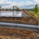 A site engineer checks a grated stormwater inlet as a buried drain pipe carries runoff from a construction site to a stable vegetated outfall.