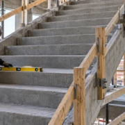 A carpenter levels a concrete stair tread while an engineer reviews the stair section, riser faces, and landing connection.
