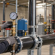 A plumbing technician checks a pressure gauge on a supported commercial water line while an engineer reviews the system drawing.