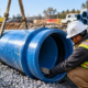Construction crew positioning a large utility pipe joint in a prepared trench while checking installation drawings.