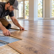 Flooring installer fitting engineered wood planks over a prepared subfloor with measuring tools in a new home.