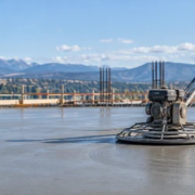 Concrete finisher uses a power trowel pan to float a fresh slab while a second worker checks the surface.