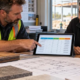 Contractor and estimator reviewing a construction pricing matrix beside building plans and material samples