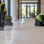 A worker vacuums a tiled corridor before laying flat protective panels to keep grit and foot traffic from damaging the new floor.