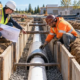 A civil engineer and pipe installer inspect a sanitary utility casing beside a protected underground trench.