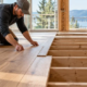 Carpenter installs timber floor planks over a framed subfloor in a house under construction.