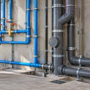 A plumbing inspector checks separate blue potable-water pipes and grey sanitary drainage lines in a building under construction.