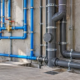 A plumbing inspector checks separate blue potable-water pipes and grey sanitary drainage lines in a building under construction.