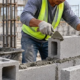 A mason lays concrete hollow blocks with their open cores visible, showing how CHB forms a wall.