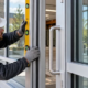 An installer checks the alignment of a commercial glass door and window frame, illustrating Division 8 openings and glazing.