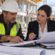 Construction project manager and insurance professional reviewing policy documents at an active jobsite