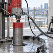 A worker uses a diamond core drill with water capture to bore a clean circular opening in a concrete slab.