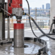 A worker uses a diamond core drill with water capture to bore a clean circular opening in a concrete slab.