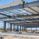 Steel frames, purlins, and metal panels form a pre-engineered metal building as a crane crew installs the roof.