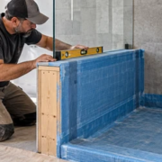 40148-feature-image Tile installer checks the waterproof membrane and level on a walk-in shower knee wall before finishing.