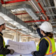 Mechanical contractors coordinate ductwork, plumbing pipes, and electrical conduit on an open commercial jobsite.
