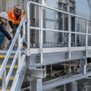 Installers inspect the guarded steel catwalk stair entry and gate while checking support brackets and the route onto the platform.