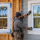 A window installer compares a new-construction window in an open framed wall with a replacement window in finished siding.