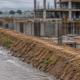 A site engineer checks a berm drain directing stormwater away from an active construction excavation.