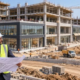 Architects and engineers review site plans beside a commercial complex with retail bays under construction