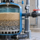 Technician checks clear outlet water beside a cutaway sand filter showing sand and gravel layers.
