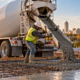 Ready-mix concrete truck pours a reinforced slab as workers guide the placement at a building site.