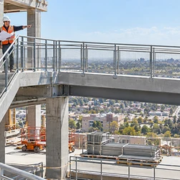 Construction supervisors check how a guarded concrete stair connects to a level pedestrian walkway on a building site.