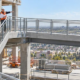 Construction supervisors check how a guarded concrete stair connects to a level pedestrian walkway on a building site.