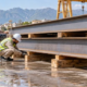 Site worker checks timber dunnage blocks supporting stored steel beams to keep materials separated and protected off the ground.