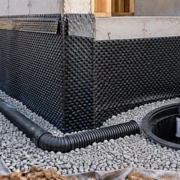 A construction crew installs perimeter drain tile and a sump system beside a waterproofed basement foundation.