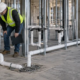 A plumber and inspector check the sanitary waste stack, branch drains, and floor drain rough-in inside a multi-unit building.