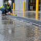 Installers align a grated trench drain across a wet commercial loading area while an engineer checks its slope and outlet.
