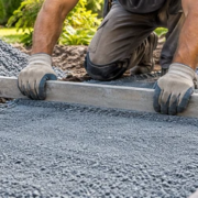 Worker levels a bed of blue stone dust beside a newly paved walkway.