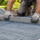 Worker levels a bed of blue stone dust beside a newly paved walkway.
